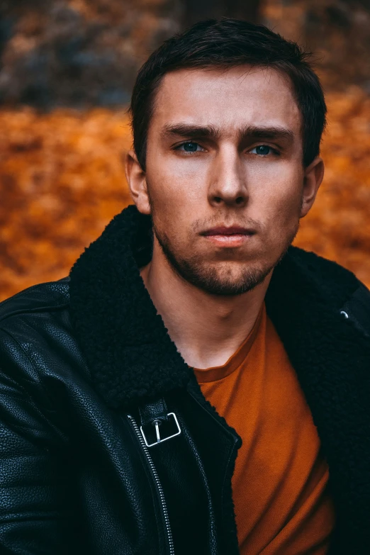 a young man wearing a brown t - shirt, black jacket and a brown shirt