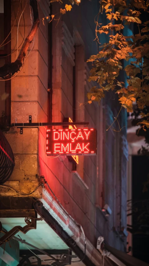 a neon sign reads dinaay emkak hanging from the side of a building