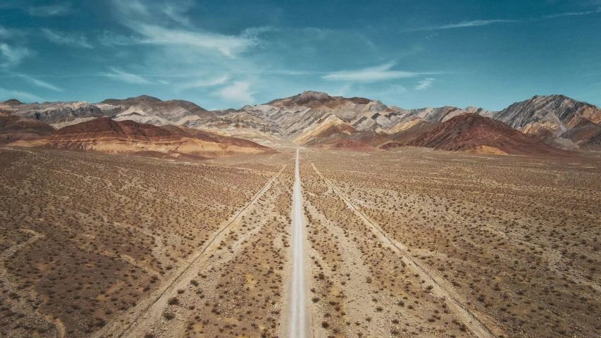 a long dirt road surrounded by hills under a blue sky