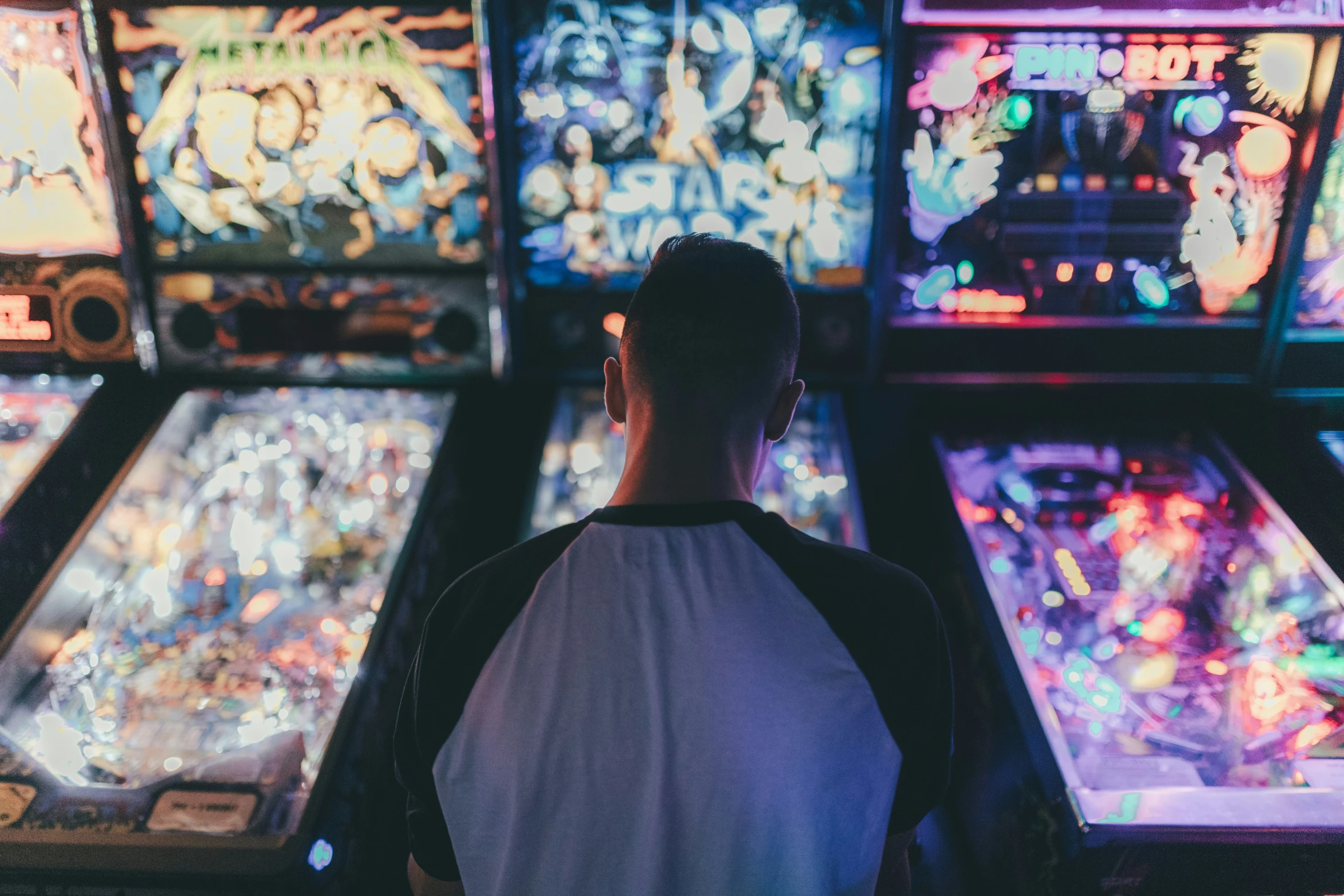 a person stands at a pinball machine and stares into the distance