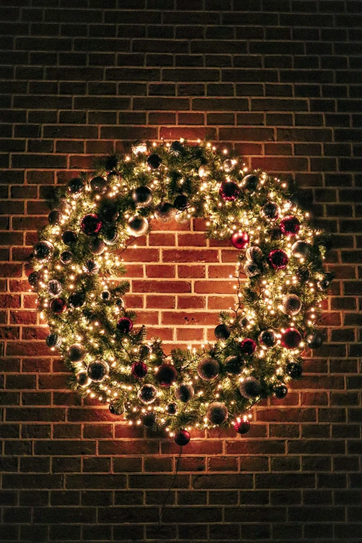 a lit christmas wreath against a brick wall