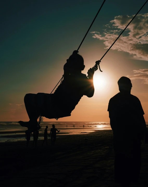 a large black silhouette of a person swinging from a string near the ocean