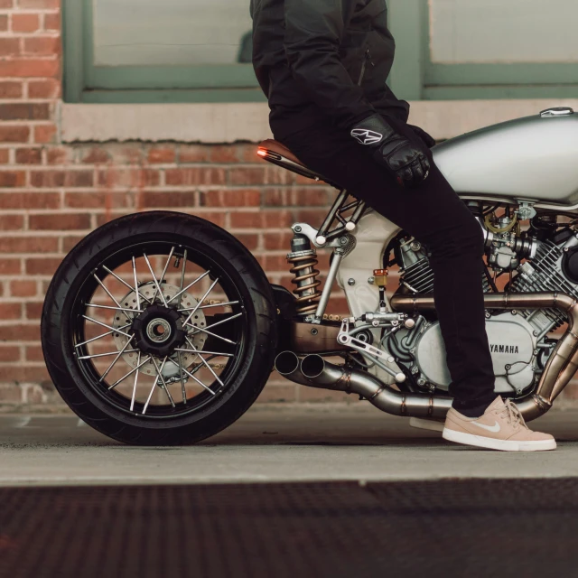 a guy standing next to his motorcycle while he wears brown sneakers