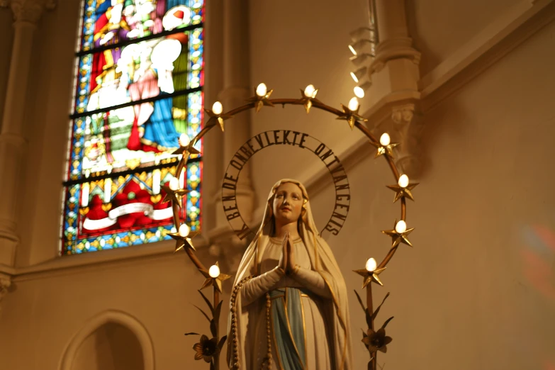 a sculpture that looks like mary magdalene is in front of the stained glass window