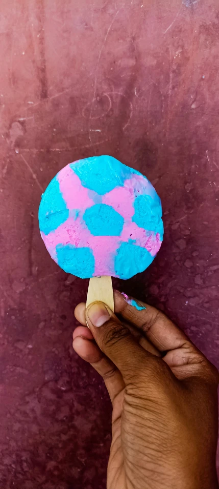 a hand holds a popsicle shaped like a ballon with blue, pink and white bubbles