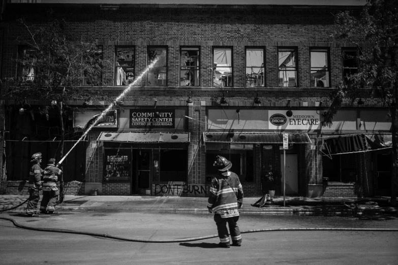 black and white po of firemen battling fire in front of brick building