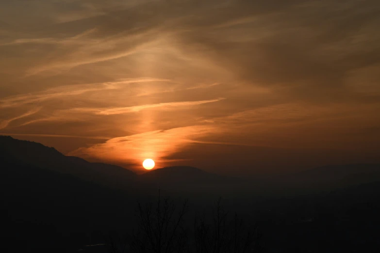 the sun setting over the mountains, with dark clouds