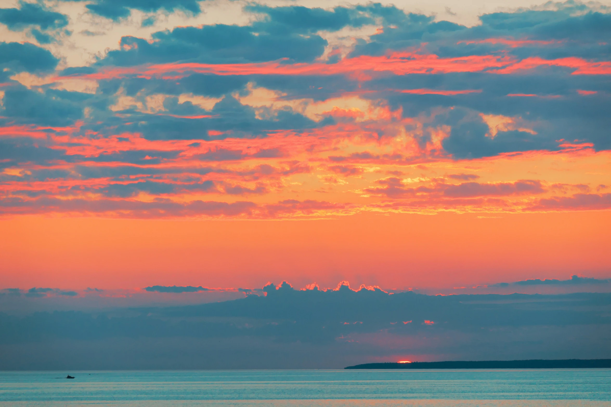 a beautiful sunrise over the ocean with a boat out at sea