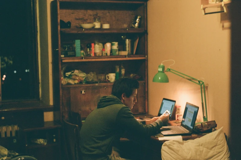 man in green sweatshirt using laptop in dark room