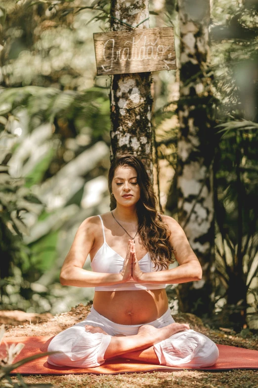a pregnant woman sitting in the forest in a yoga pose