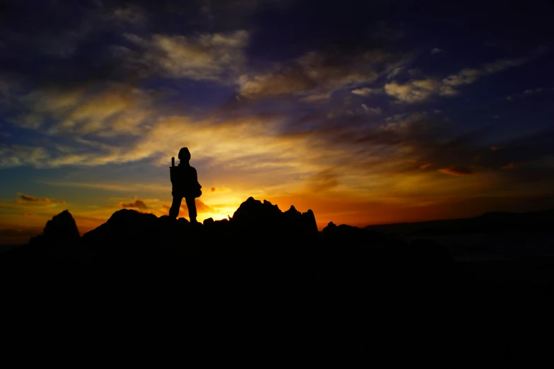 the silhouette of a man standing on rocks and arms outstretched as the sun rises in the distance