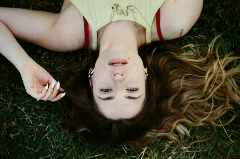 a woman laying in the grass while holding a cigarette