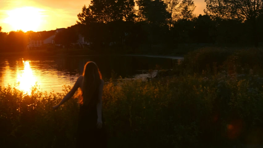 a woman standing on top of a lush green field next to a lake