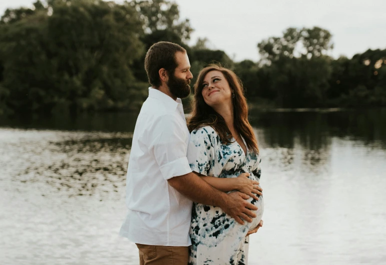 a couple cuddles next to a lake at sunset