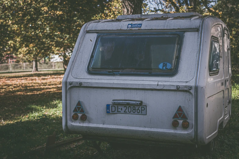 an old white camper sits in front of some trees