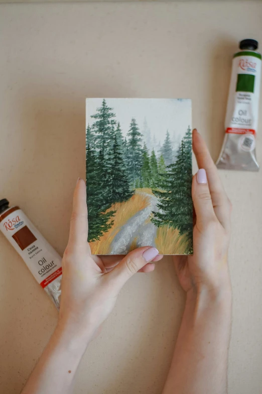 two hands holding a painting over some items that are used to create paintings