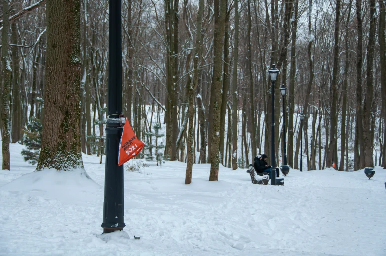 the park bench is covered with snow and has two people near it