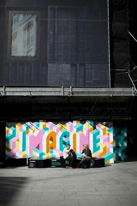 people sitting on benches underneath a mural on a building