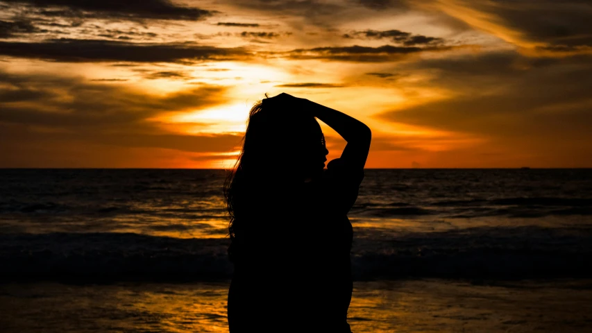 a woman stands at the edge of a beach as the sun sets