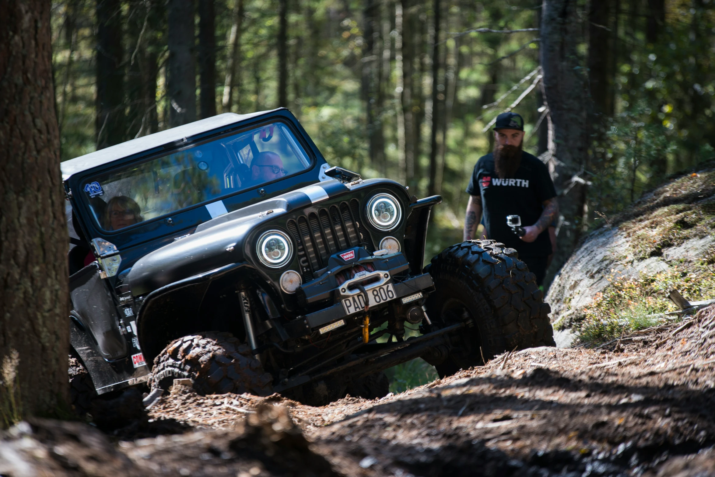 two men stand next to a jeep in the woods