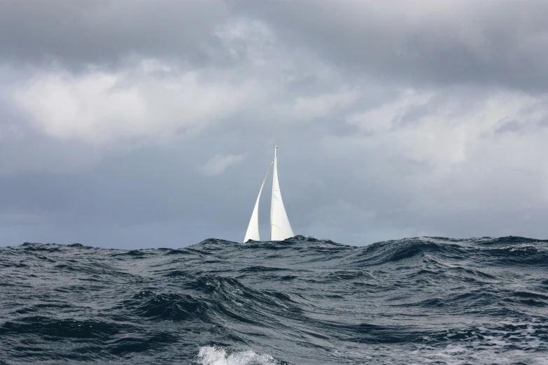 a sail boat in the ocean under a cloudy sky