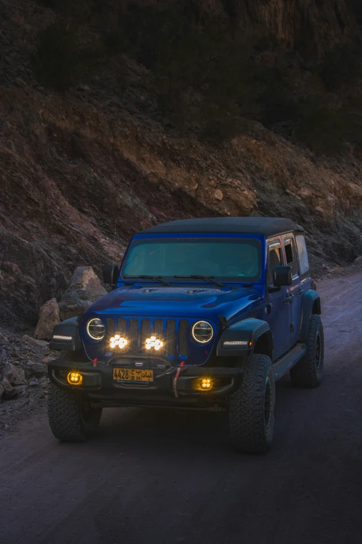 blue jeep with bright headlights on roadway near rocky area