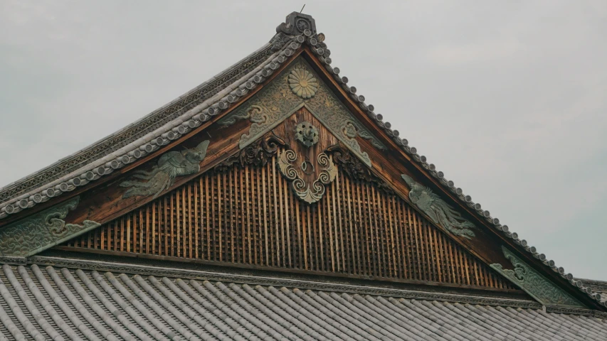 an intricate roof with wooden tiles against a cloudy sky