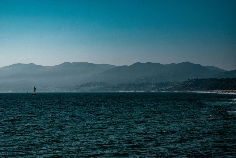 sailboat sailing along the ocean near a mountainous coastline