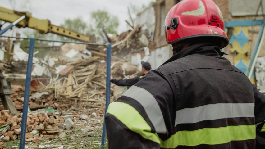 man in a fire fighter uniform and a helmet looking at the rubble