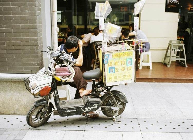 man sitting on motorbike by an outdoor bakery