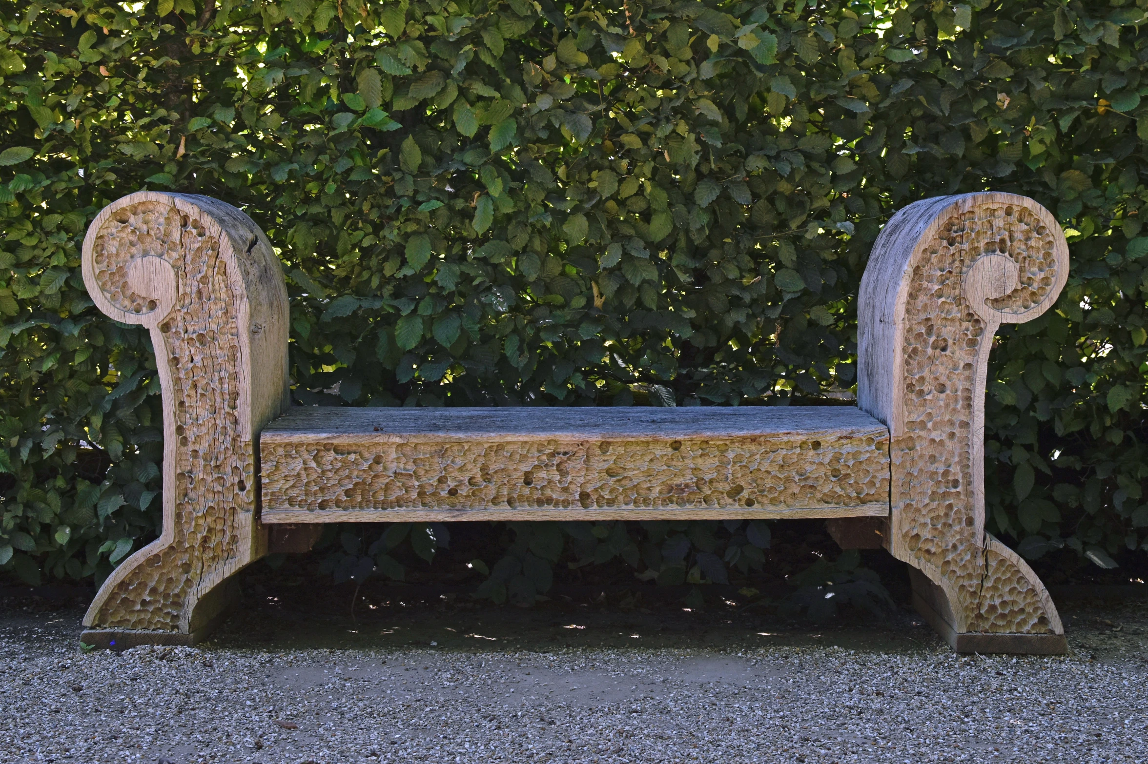 a decorative bench sitting in front of a green bush