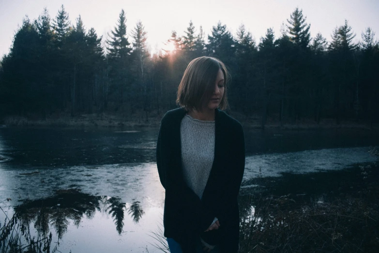 there is a woman standing near water with trees in the background