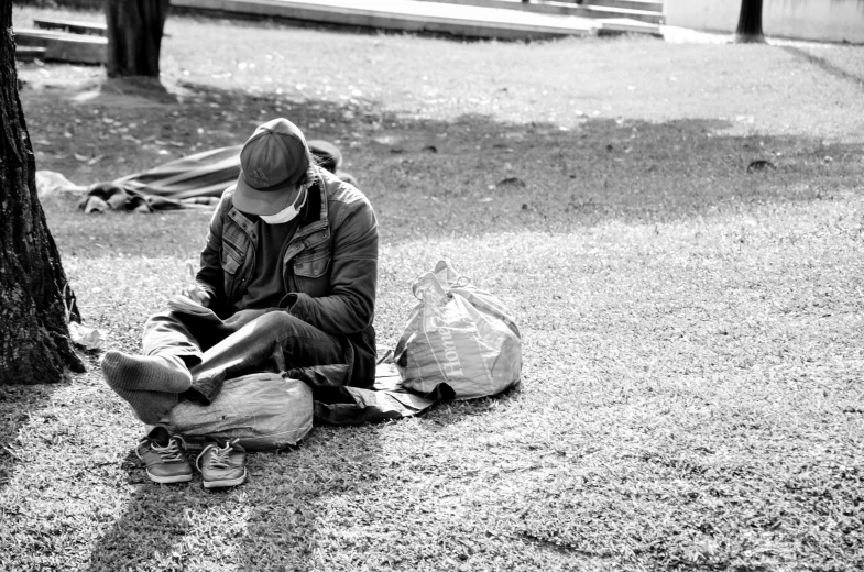 a man in a hat sitting against a tree looking at his cell phone