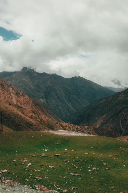 a green grassy field in the mountains is next to a river