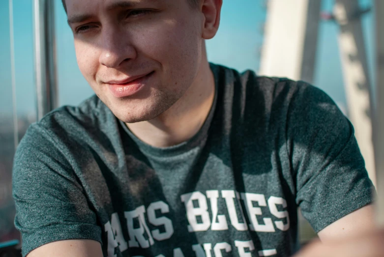 a man in grey t - shirt sitting next to a wall