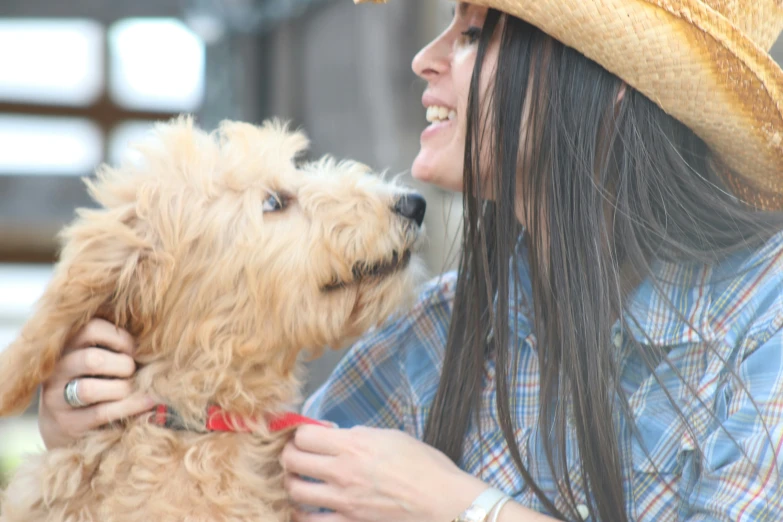 a woman holding a tan dog wearing a cowboy hat