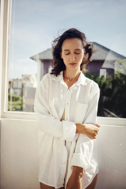 a woman is wearing a white shirt next to her window