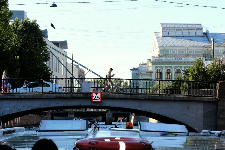 two people crossing a bridge with a red boat on the back