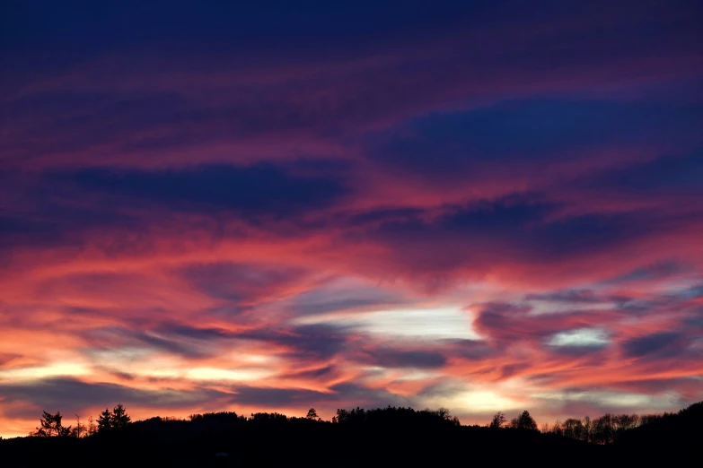 a red and pink sky with many clouds above a forest