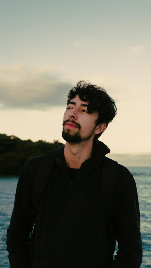 a man with glasses standing by the ocean