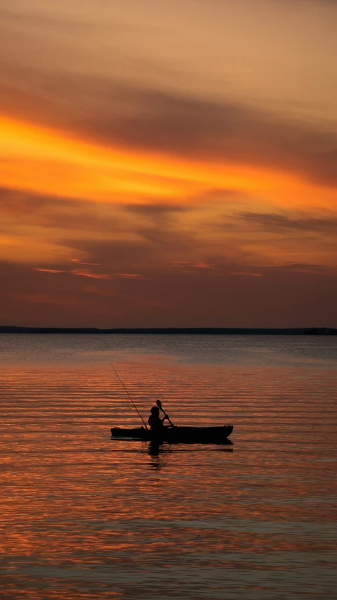 the man rows his canoe with a beautiful orange sunset