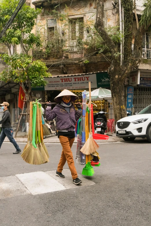 an asian woman walking across a road carrying several brooms