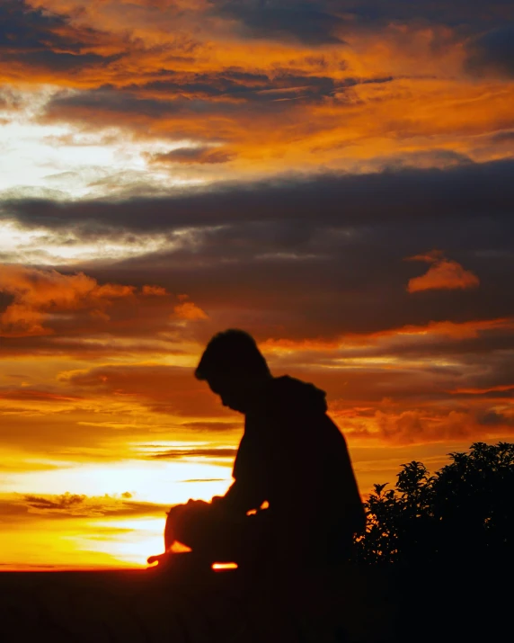 the silhouette of a man sitting in front of a sunset