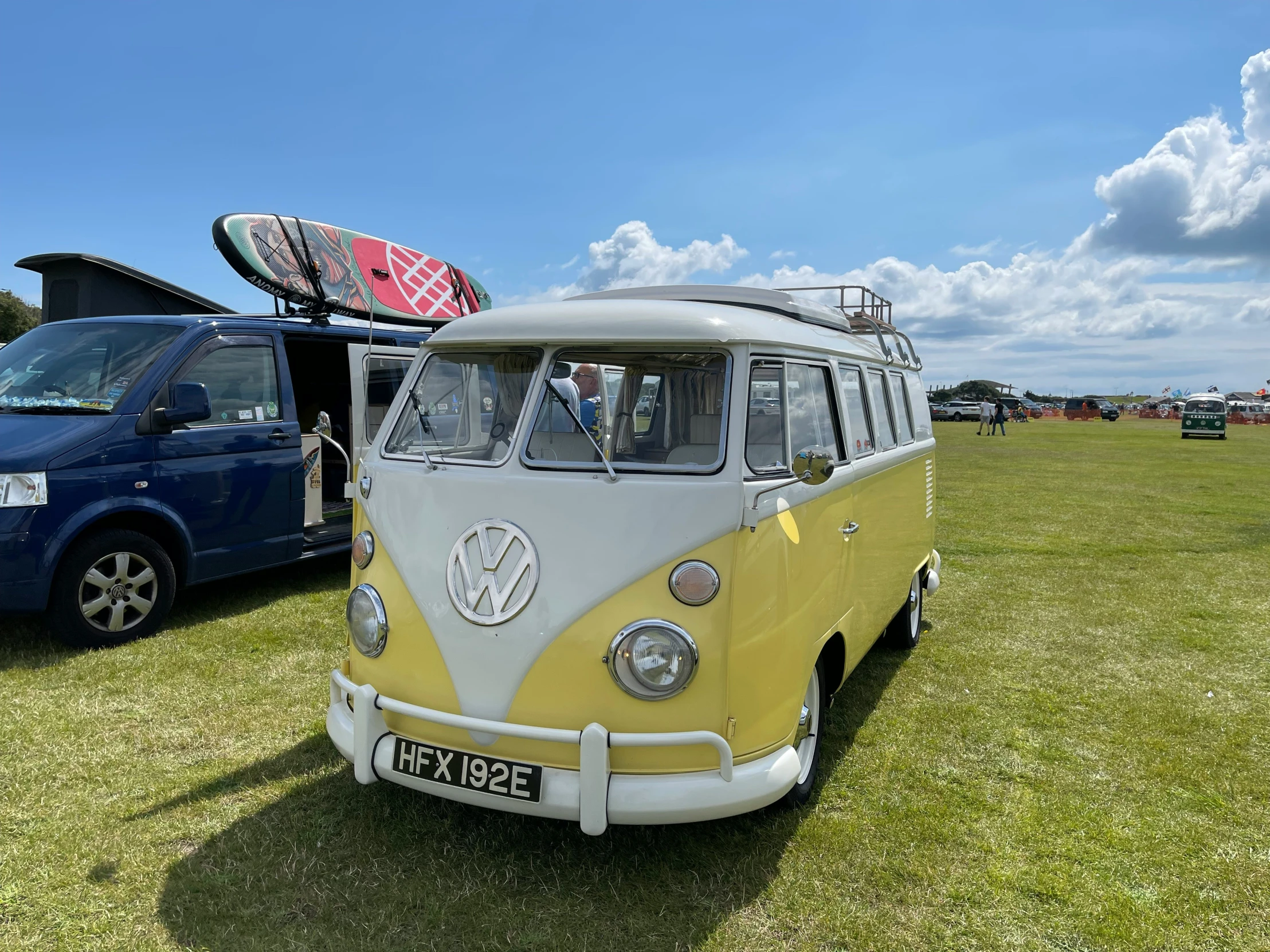 a vw bus parked on the grass with other vehicles in the background