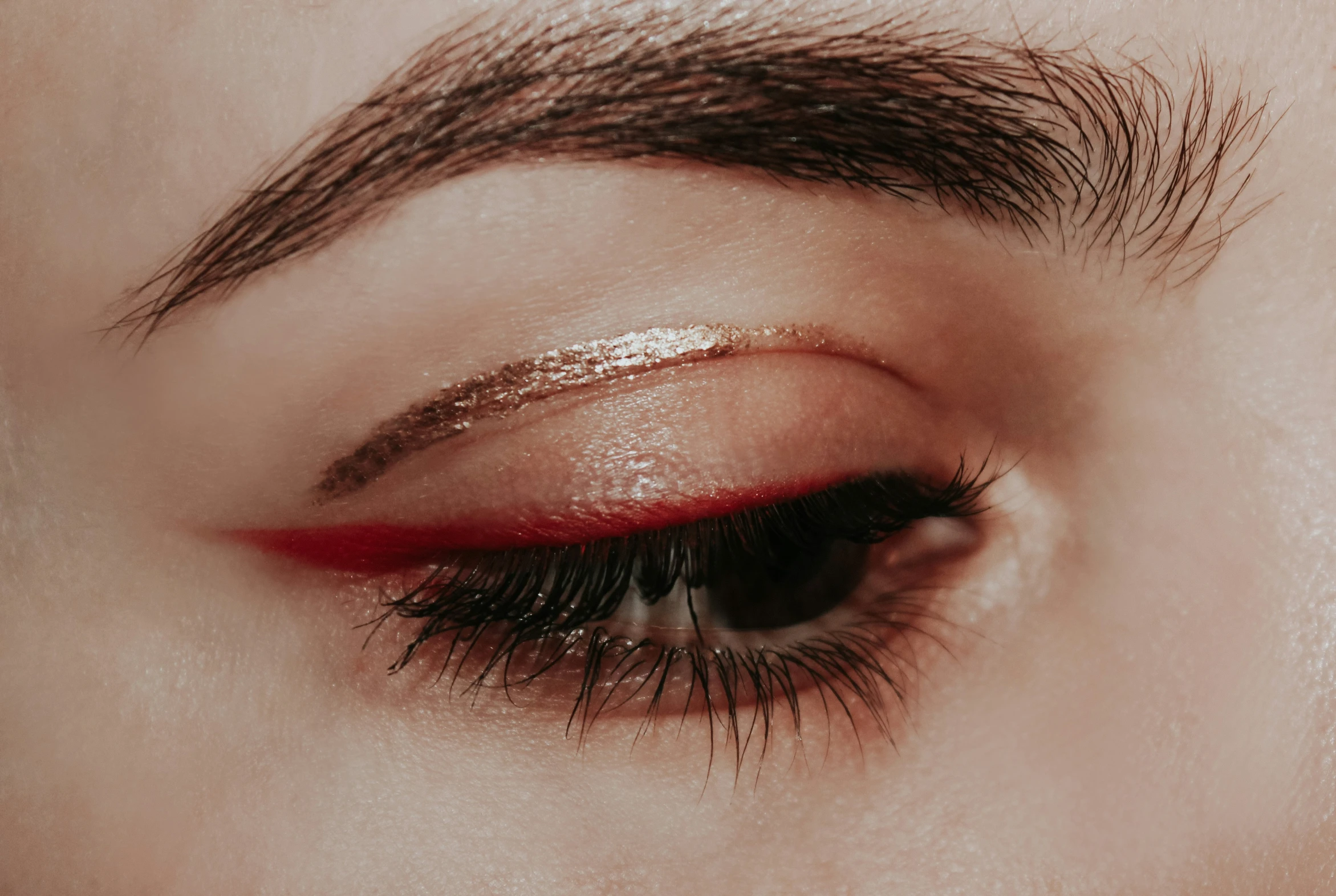 a woman's eye with gold and red colored lashes