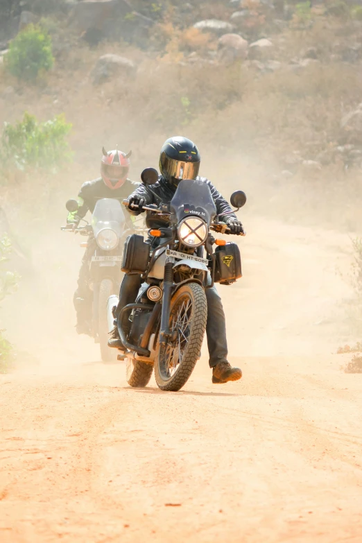 two people riding on motorcycles in the dirt