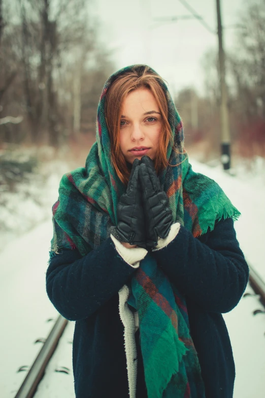 a woman with brown hair and winter clothes covers her mouth in a snowy area