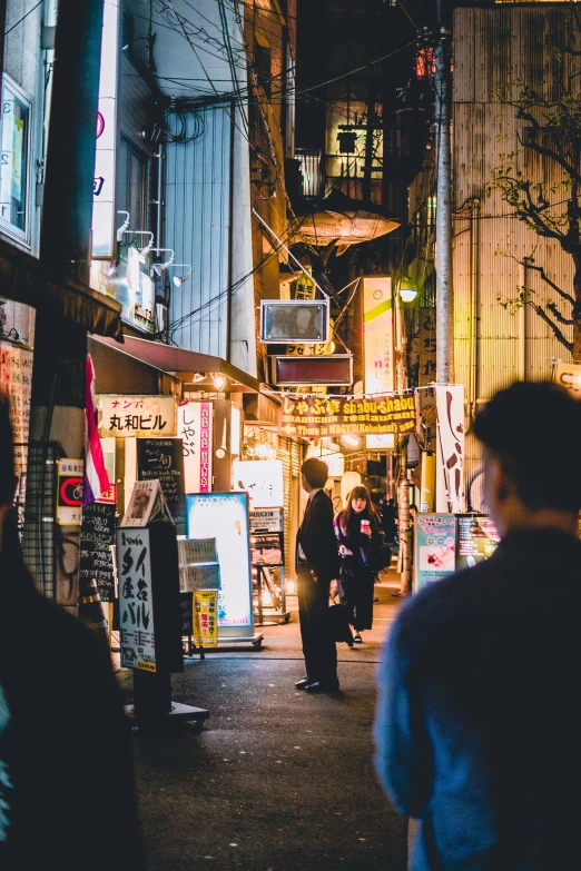 a narrow street at night with signs and people