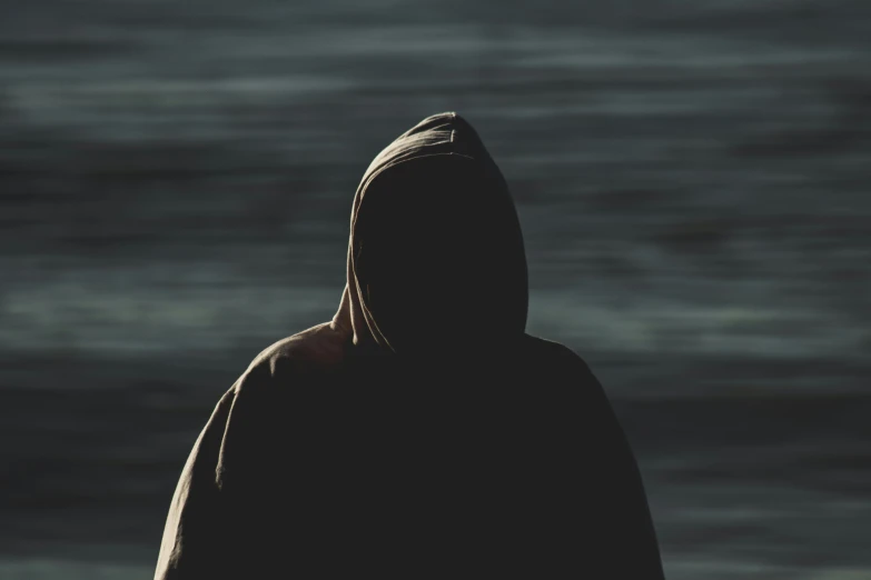 hooded person looking out to the ocean from a rocky shore