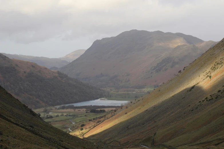 a grassy mountain side valley, with some water and mountains in the background